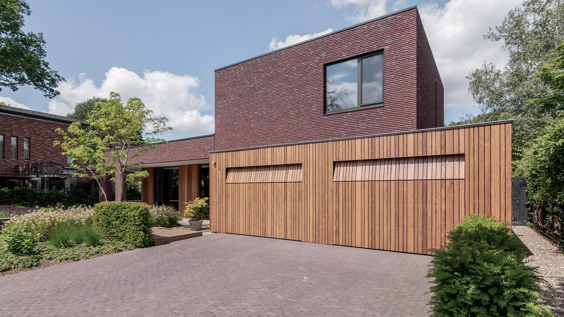De houten garagedeuren zijn onopvallend ingebouwd in het ontwerp van de gevelbekleding