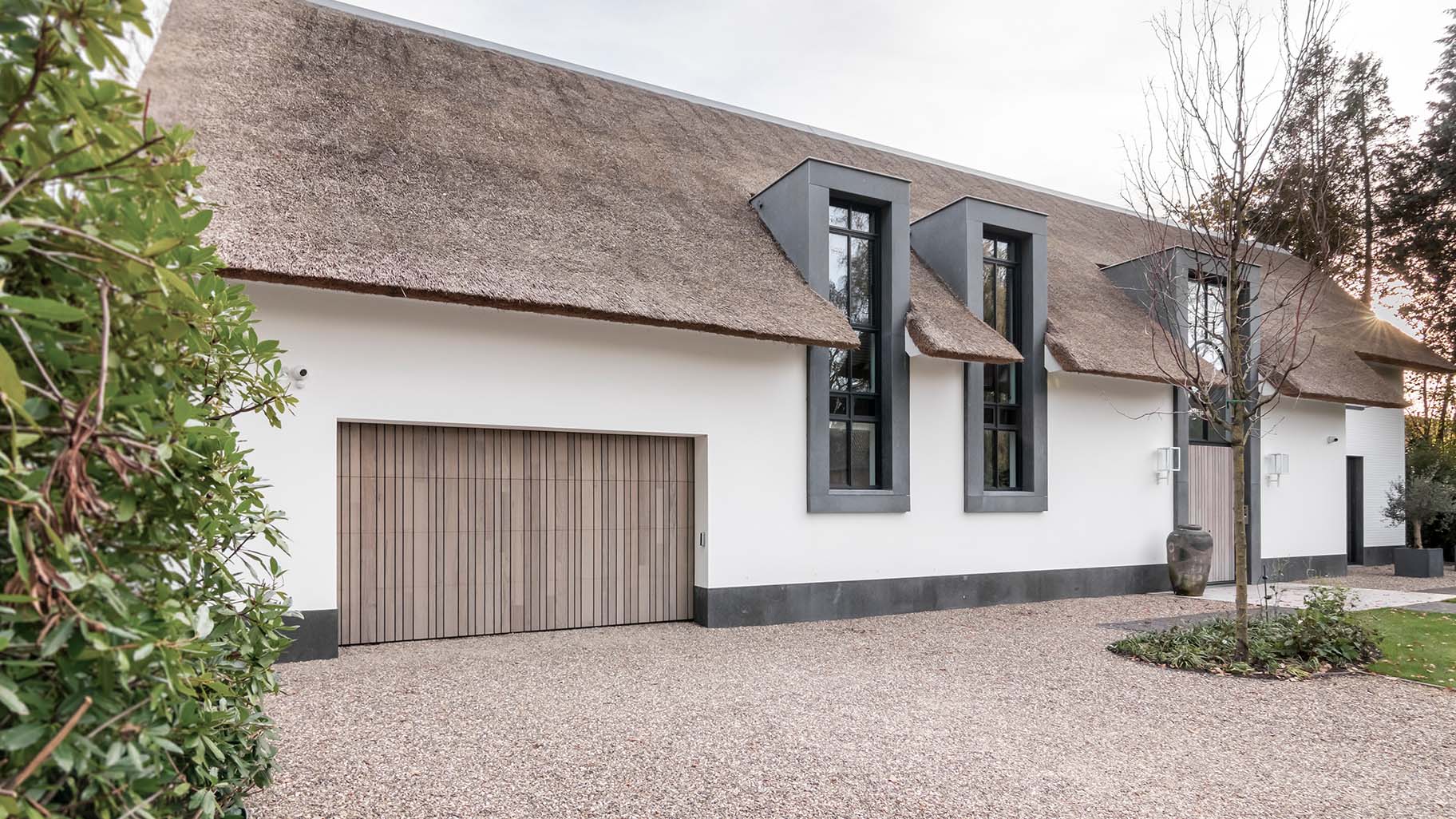 Landelijke woning met rieten dak en houten garagedeur achter de dag voor een harmonieuze uitstraling