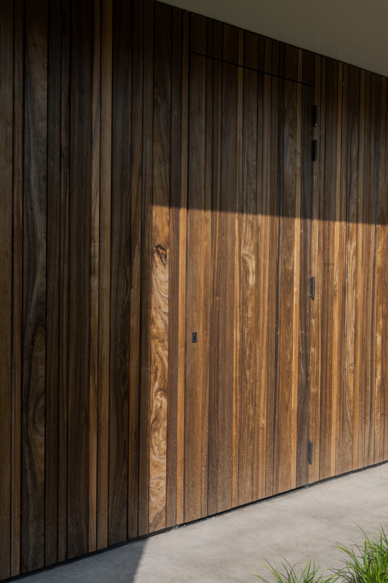 Twee houten garagedeuren uitgevoerd in padoek en perfect geïntegreerd in de verticale houten latten bij deze prachtige nieuwbouwwoning aan het water
