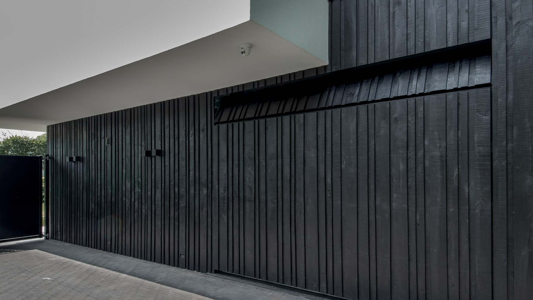 Zwarte houten garagedeur met verticale latten in drie breedtes, naadloos geïntegreerd in de gevel